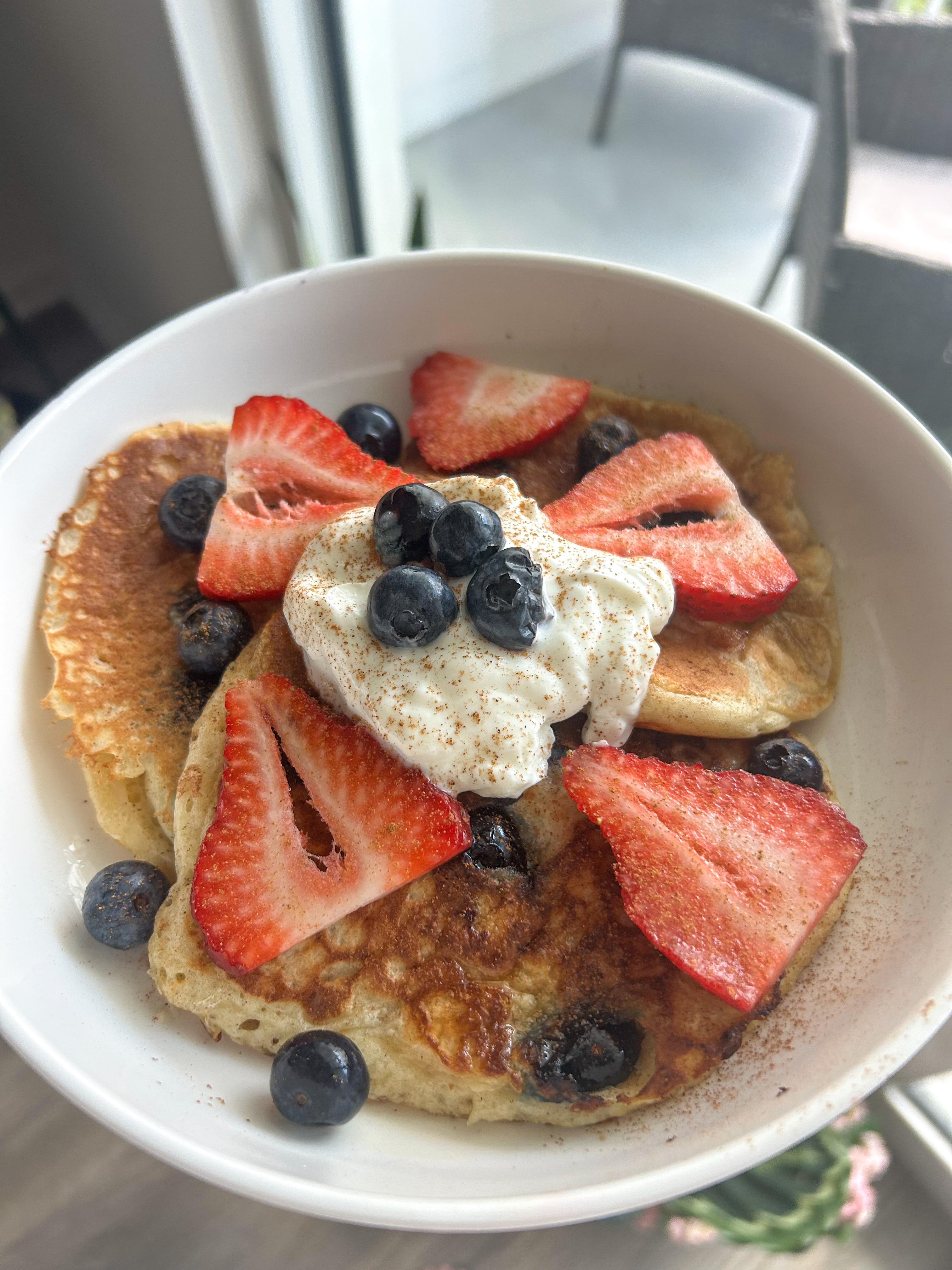 A bowl of pancakes topped with sliced strawberries, fresh blueberries, a dollop of Greek yogurt, and a sprinkle of cinnamon.
